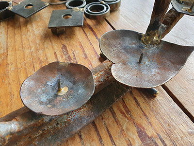 An image of a recycled metal candelarba. The candelarbra is made from rusty harrows that have been left lying on a local farm for decades. Old steel is good steel.The candle holders and made from recycled library shelves, cut shaped and drilled for the nail to position the candle on. Welded by Graham Hughes of McKinley Rd Creatives using a variety of welding processes